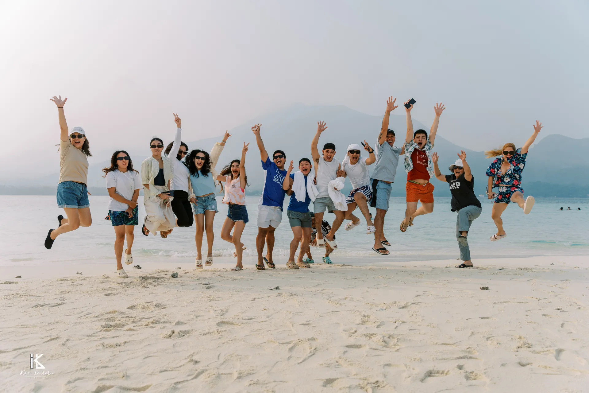 AMZ team members with arms raised on the White Island sandbar, with Camiguin's mountains behind them