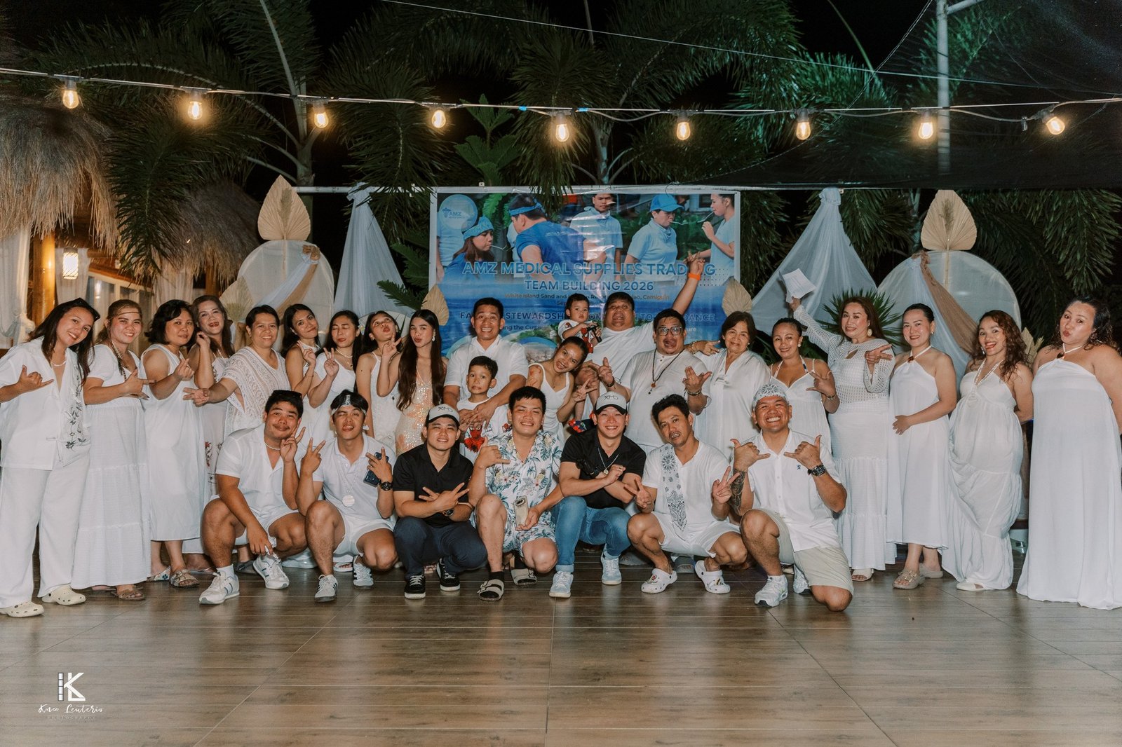 The whole AMZ team dressed in white, posing in front of the Team Building 2026 banner under string lights