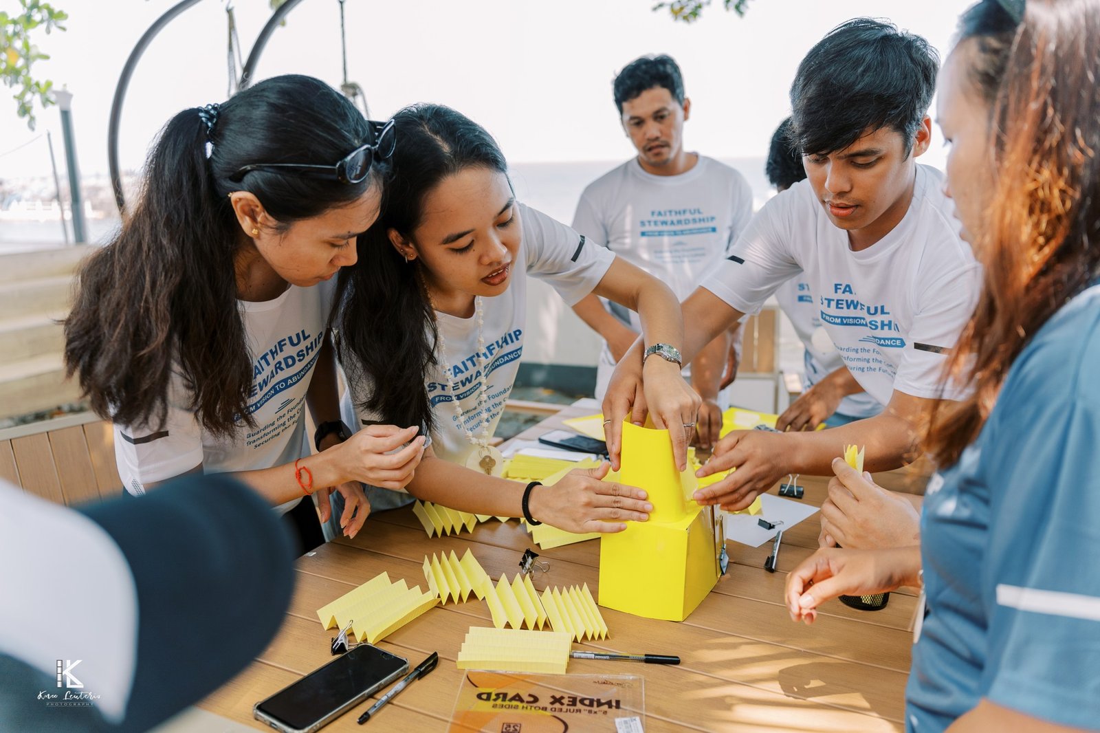 Team members in Faithful Stewardship shirts building a tower out of yellow index cards