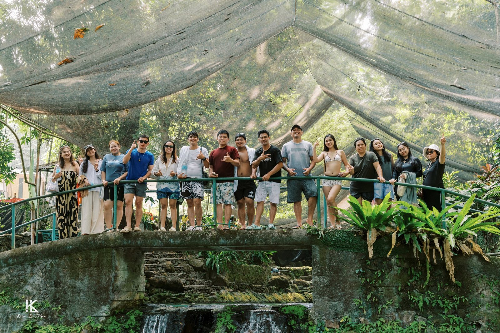 The AMZ team waving from a stone bridge above a cold spring pool, under a net canopy